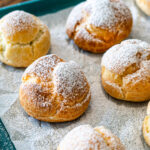frozen mini profiteroles dusted with powder sugar on a baking tray