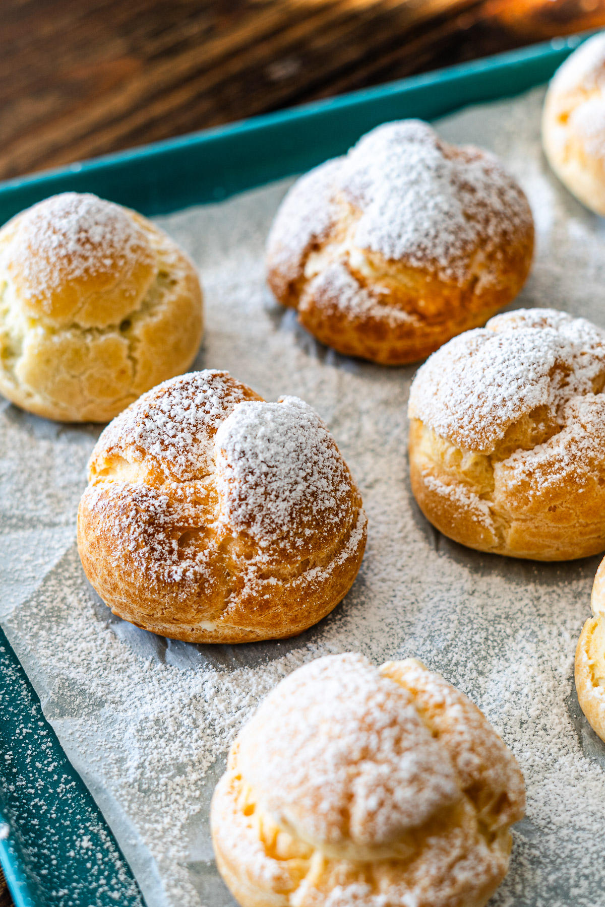 frozen mini profiteroles dusted with powder sugar on a baking tray
