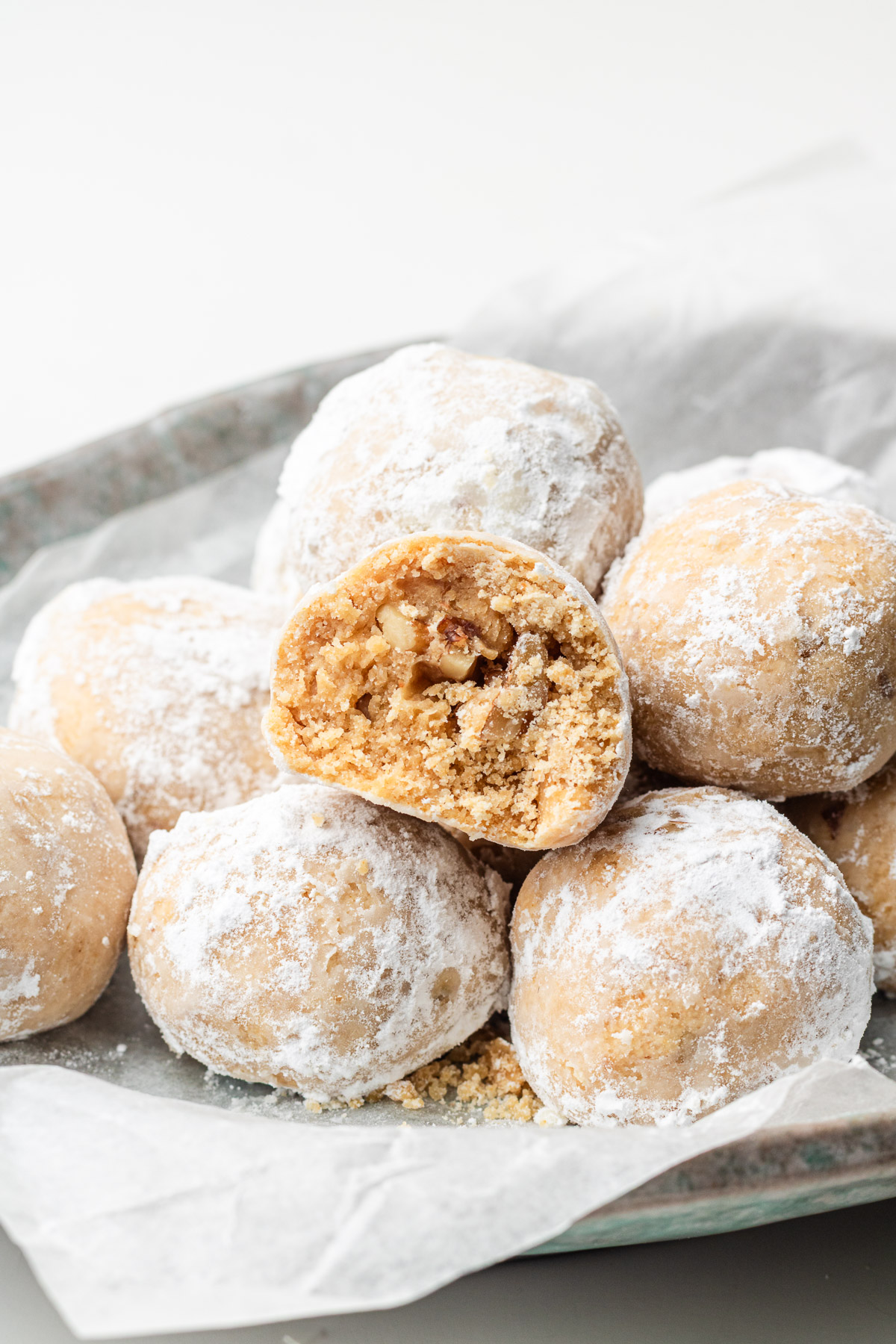 kinako cookies with walnuts coated in powdered sugar cut in half on a parchment lined shallow bowl