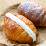cinnamon roll salt bread piped with cream cheese whipped cream on a plate lined with parchment paper