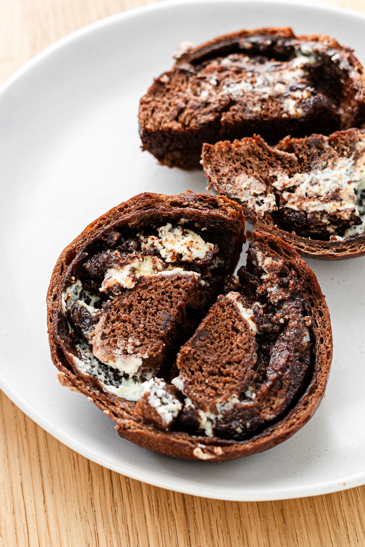 cream cheese and chocolate chip stuffed chocolate bagel sliced in half on a white plate