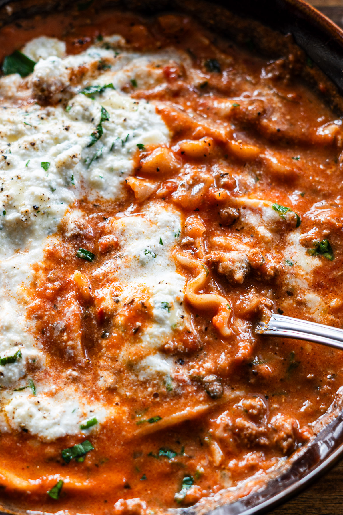 spoon picking up lasagna soup with herby scallion ribotta