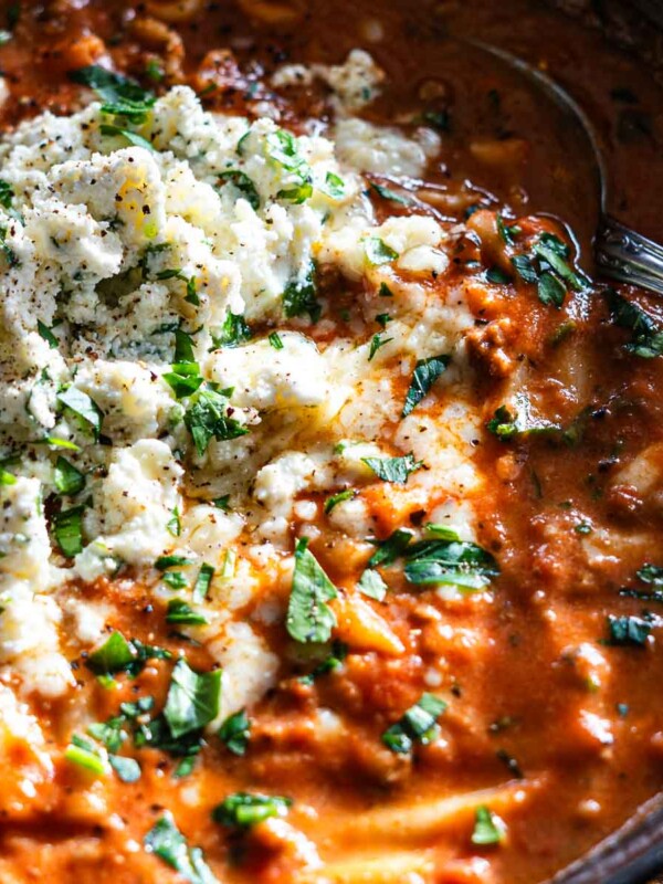 spicy lasagna soup in a bowl topped with herb scallion ricotta in a brown bowl