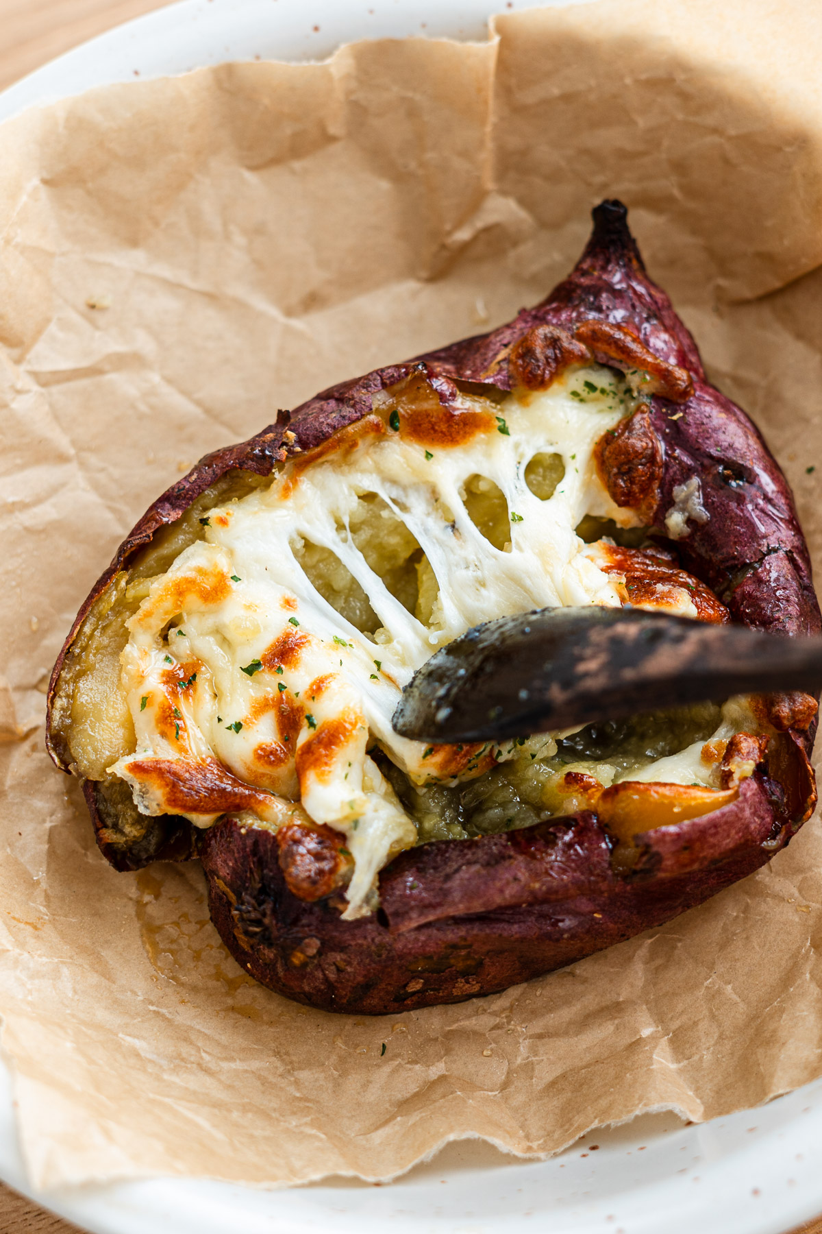 air fried japanese sweet potato topped with cheese, butter and honey with a spoon pulling cheese