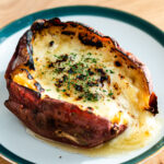 japanese sweet potato stuffed with cheese and topped with honey and dried parsley on a green rimmed dessert plate