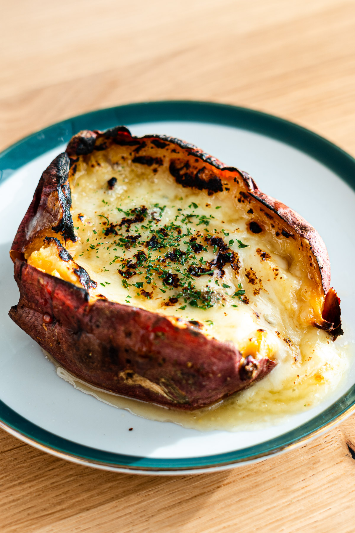 japanese sweet potato stuffed with cheese and topped with honey and dried parsley on a green rimmed dessert plate