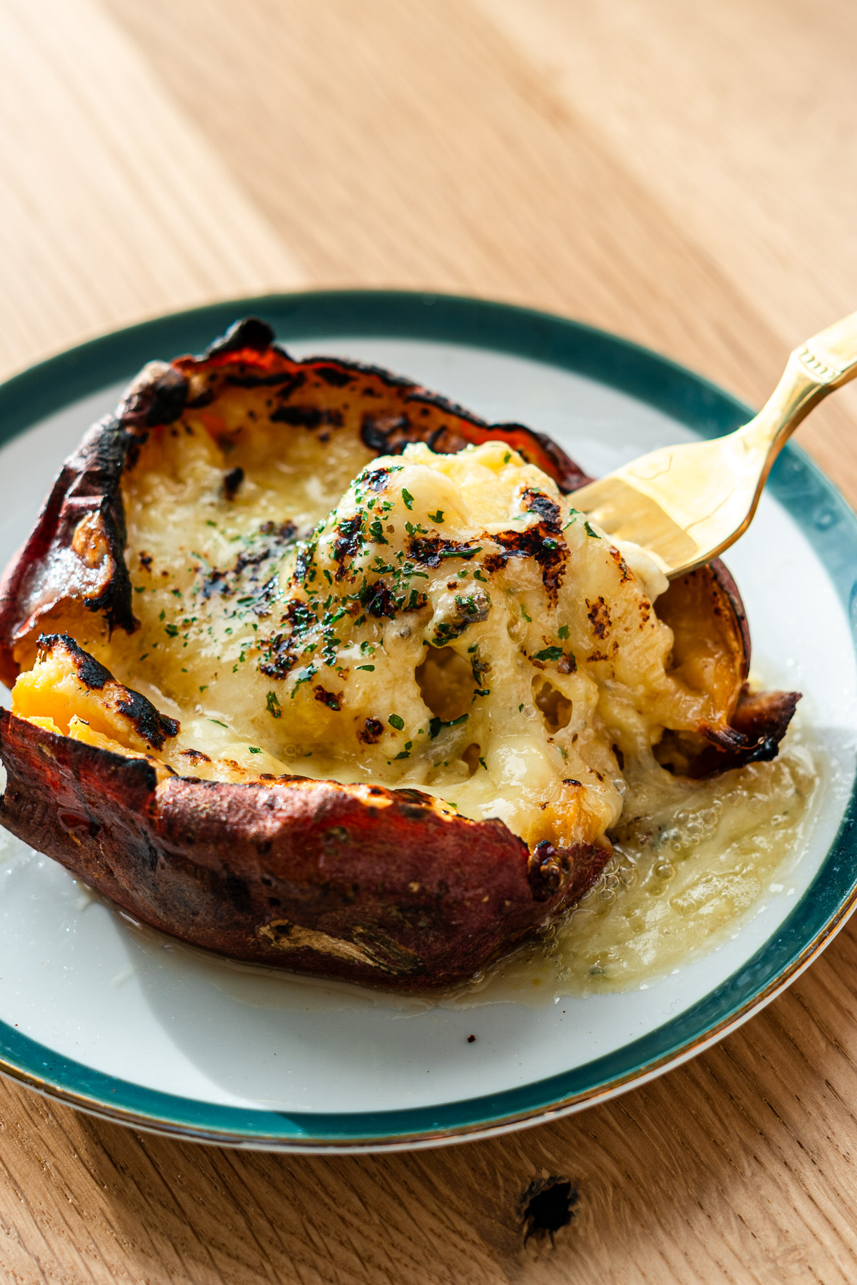 japanese sweet potato stuffed with cheese and butter topped with honey and dried parsley on a green rimmed dessert plate with fork lifting the cheese