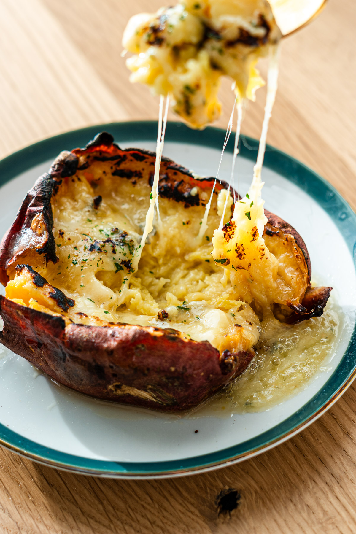 cheesy honey butter japanese sweet potatoes on a dessert plate with a fork lifting the cheese pull