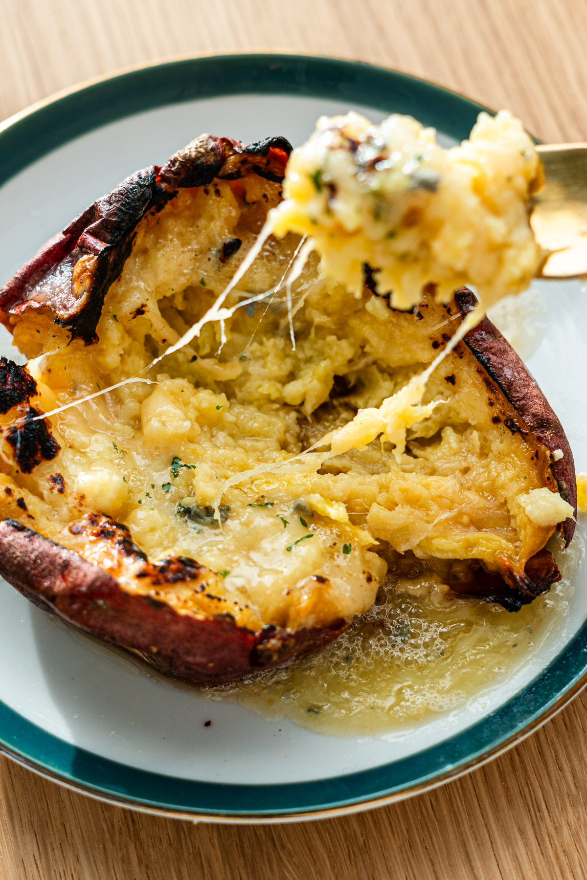 cheese stuffed japanese sweet potato on a rimmed green plate with fork scooping out the sweet potato and cheese