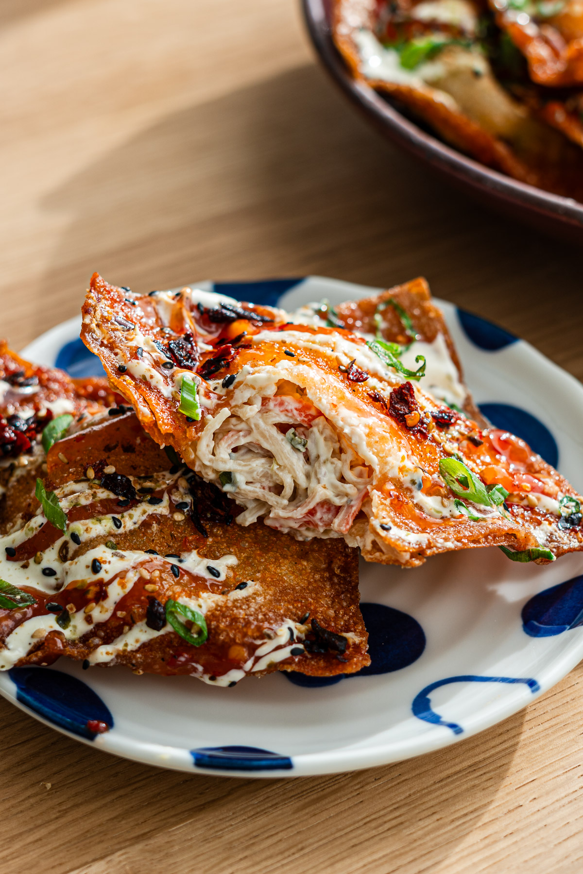 bite taken out of stuffed crab rangoon wonton nachos on a blue plate