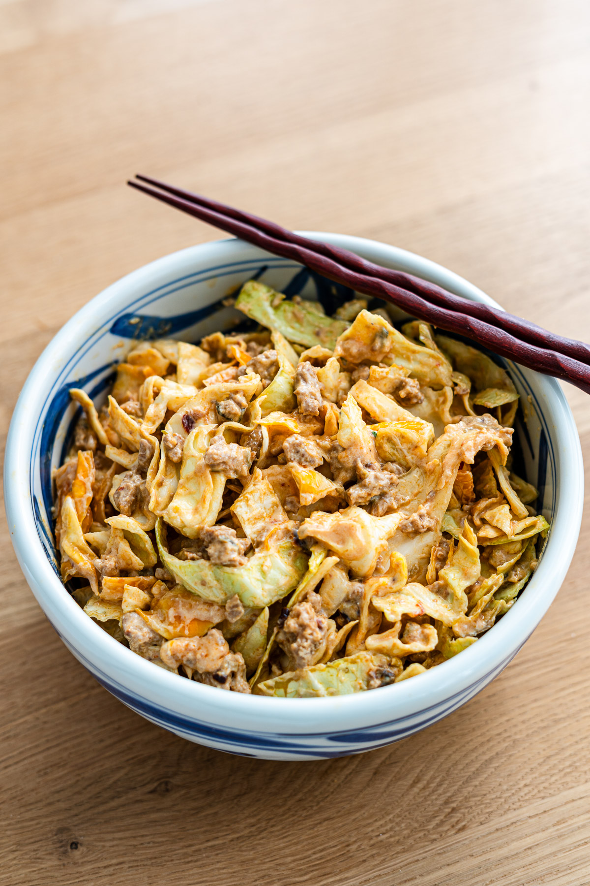 cabbage salad mixed with creamy tofu dressing and spicy pork mince in a large blue bowl