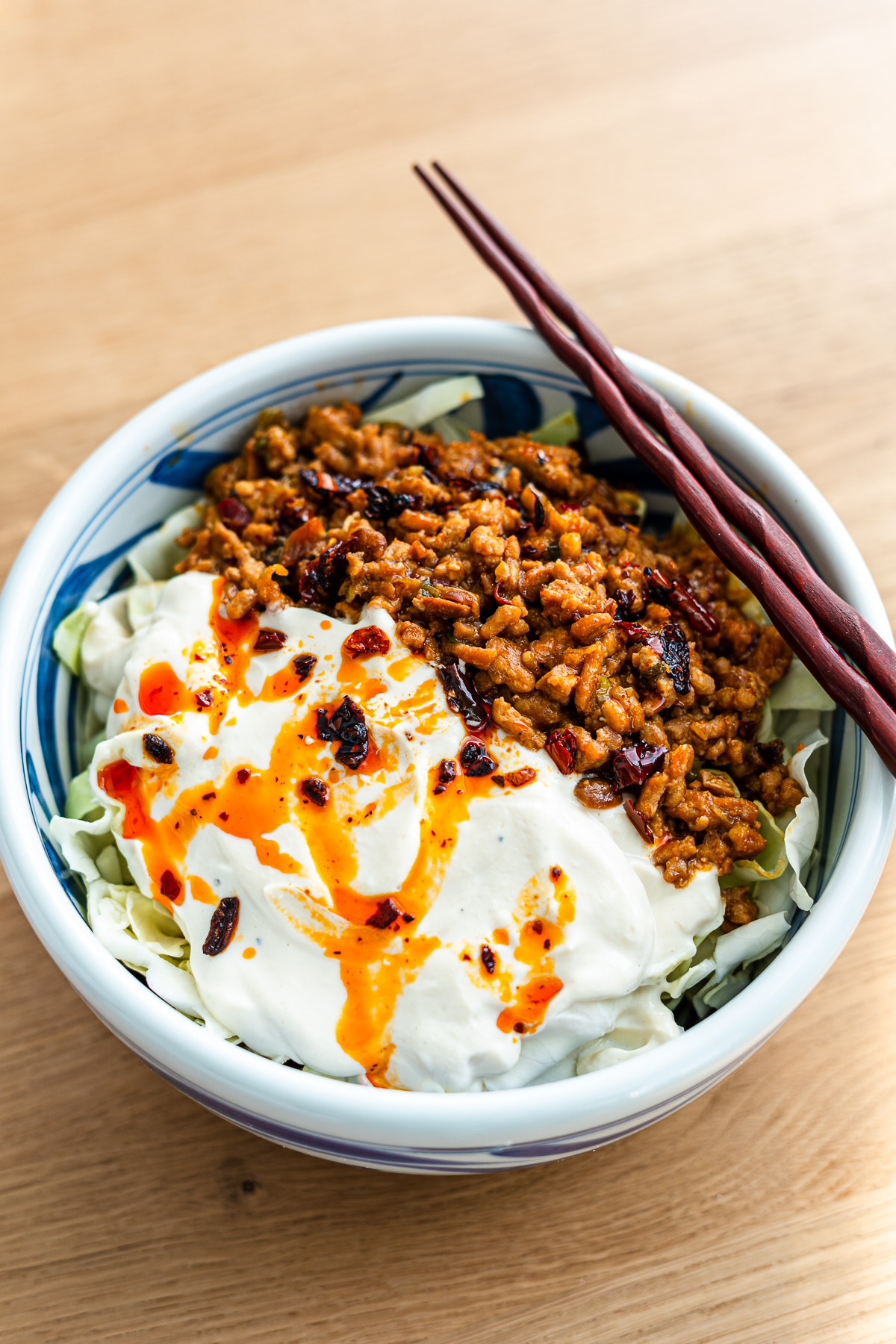 creamy mapo tofu cabbage salad in a blue bowl drizzled with chili crisp