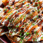 crispy wonton crab rangoon nachos drizzled with sweet chili sauce, spicy mayo, chili crispy, sesame seeds, furikake and scallions on a purple plate