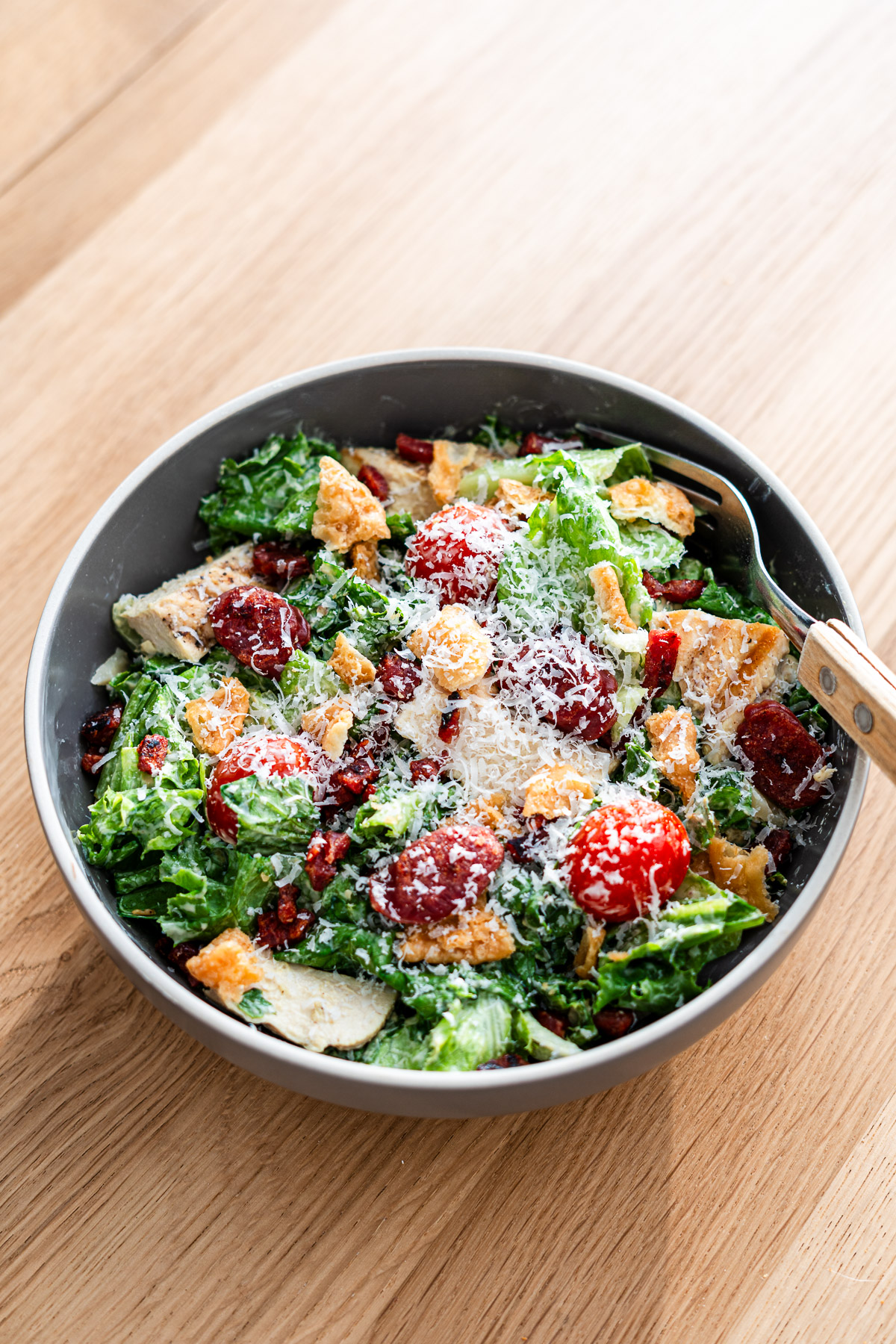 caesar salad with lap cheong, lettuce, tomato, grilled chicken and fried wonton chilps in a brown bowl