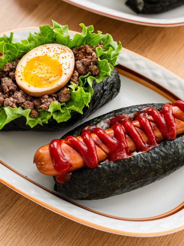 onigiri dog (rice dog) with sausage, ketchup, soft boiled egg, miso niku and lettuce on a white oval plate