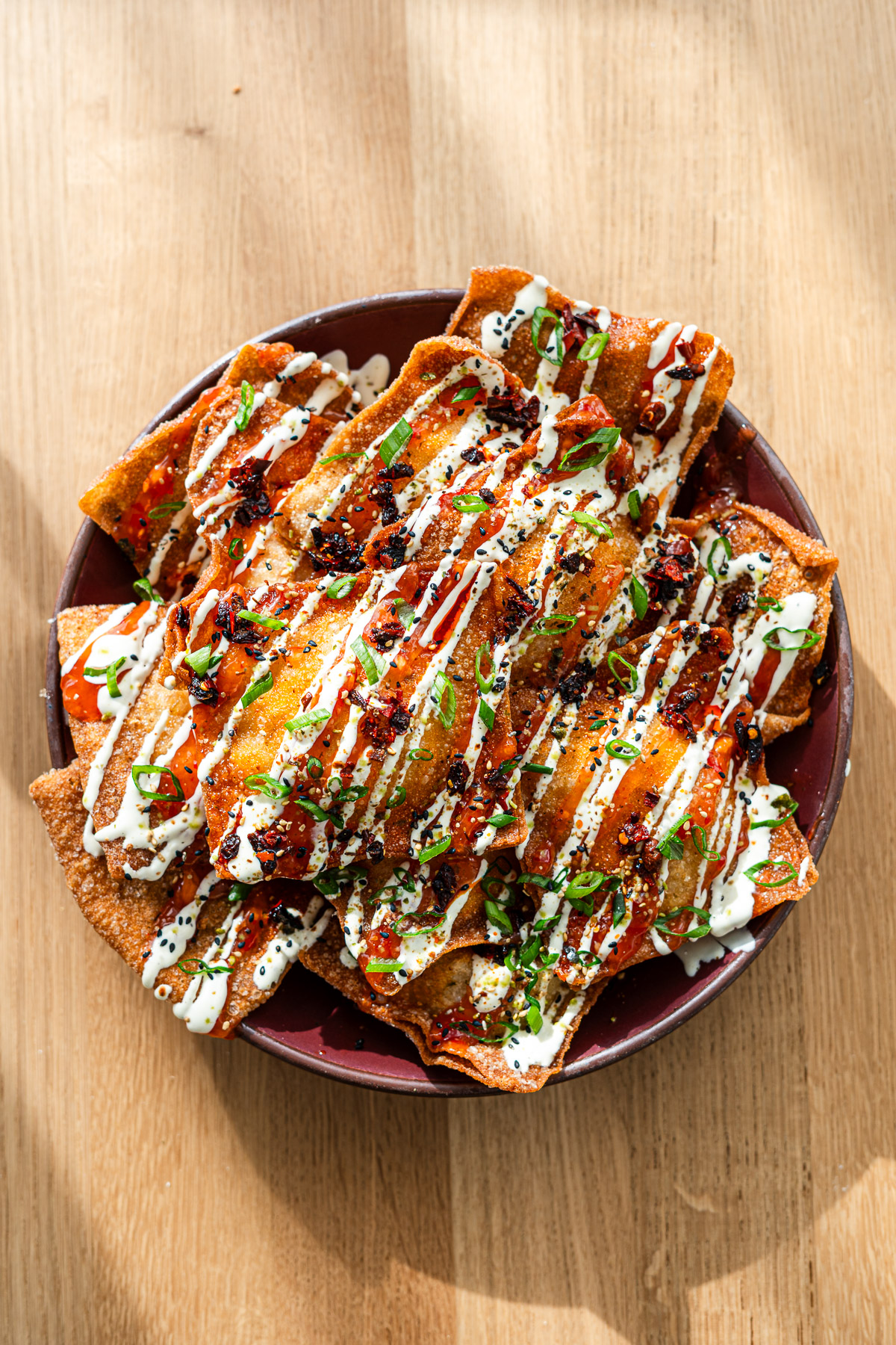 crab rangoon stuffed wonton nachos on a plate drizzled with sweet chili sauce, wasabi mayo, scallions, sesame seeds, chili oil and furikake