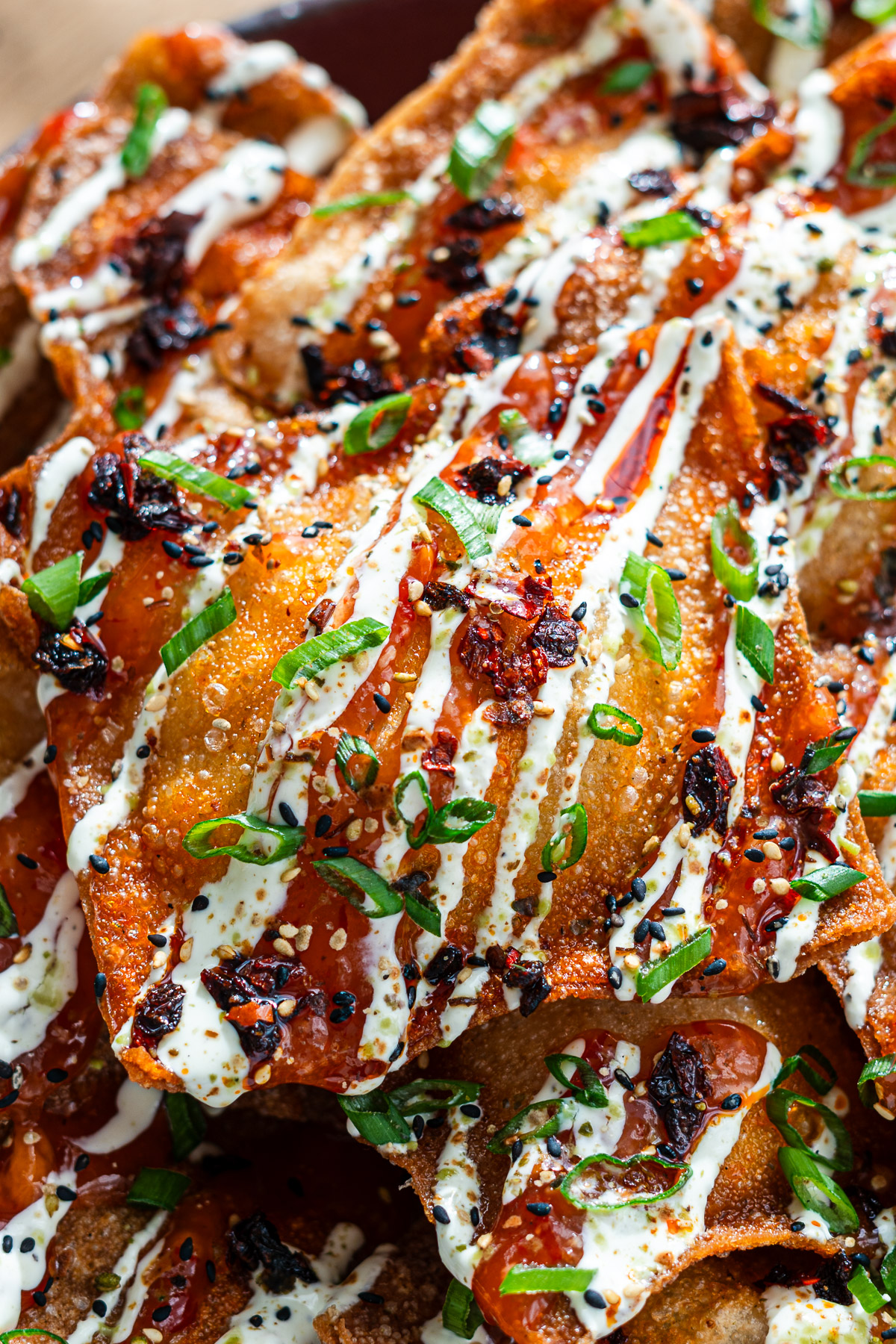 close up crab rangoon wontons on a purple serving plate drizzled with sweet chili sauce, chili crisp, spicy mayo, furikake, sesame seeds and green onions
