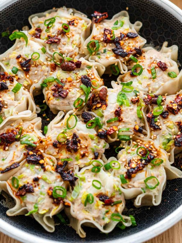 viral no fold blanket dumplings on a black 8 inch frying pan topped with scallions, chili crisp oil and sesame seeds