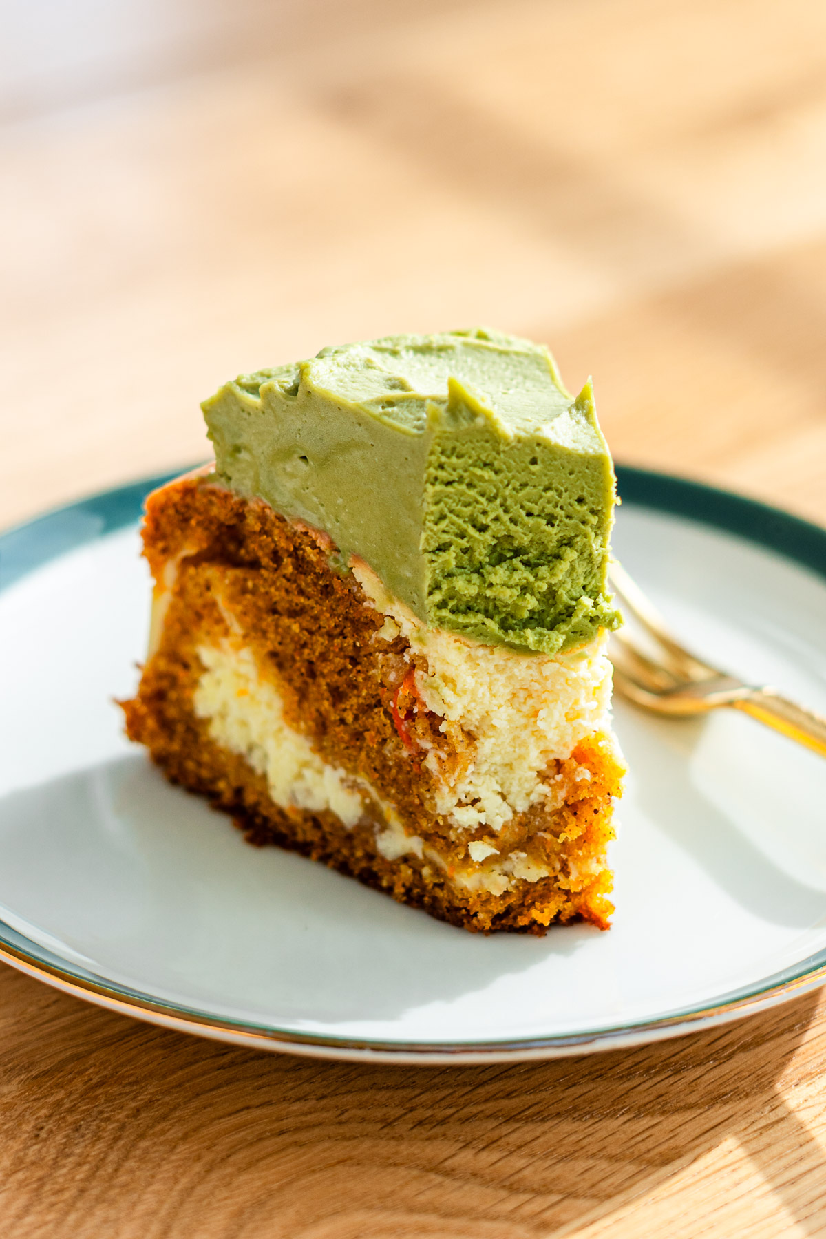 baked carrot cake cheesecake topped with matcha cream cheese frosting on a green rimmed dessert plate with a bite taken out of it