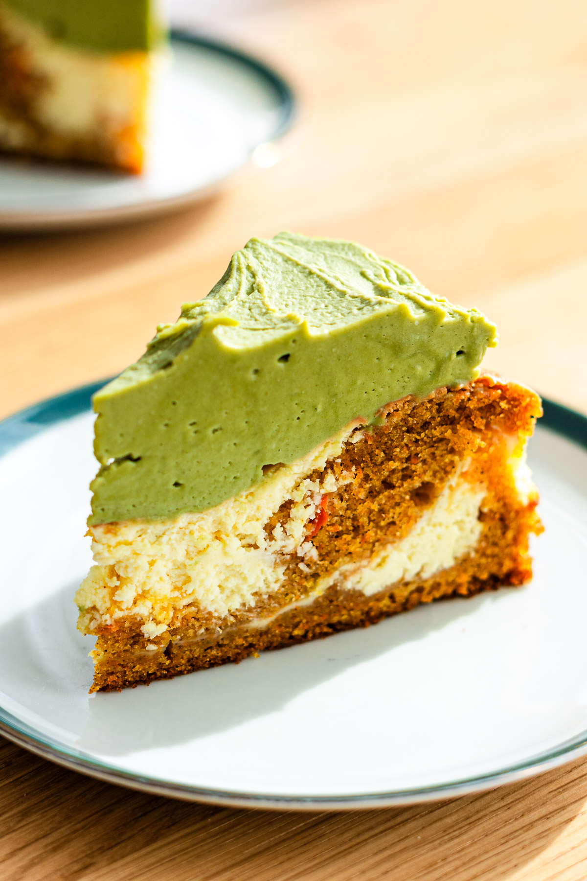 carrot cake swirled with cheesecake and topped with matcha cream cheese frosting on a green rimmed dessert plate