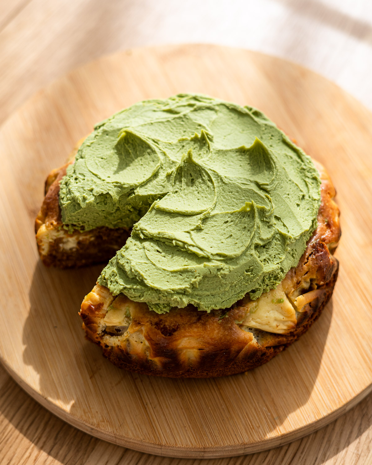baked carrot cake cheesecake on a wooden cutting board topped with matcha cream cheese frosting