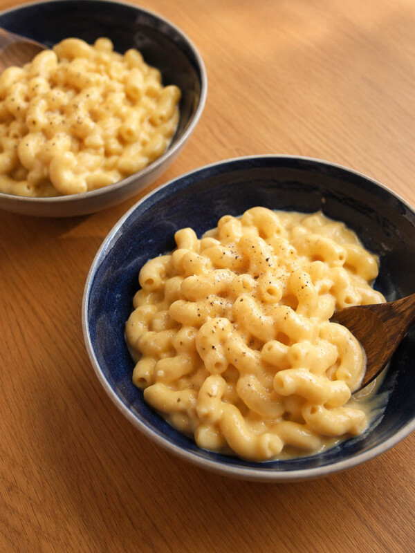 2 bowls of creamy cottage cheese mac and cheese in a dark blue bowl with a white rim with a wooden spoon on the side