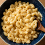 high protein cottage cheese mac and cheese in a dark blue bowl with a white rim with a wooden spoon on the side, close up shot