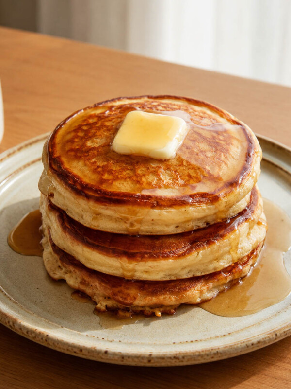 stack of crispy edged fluffy cottage cheese pancakes on a ceramic plate with melty piece of butter on top and maple syrup
