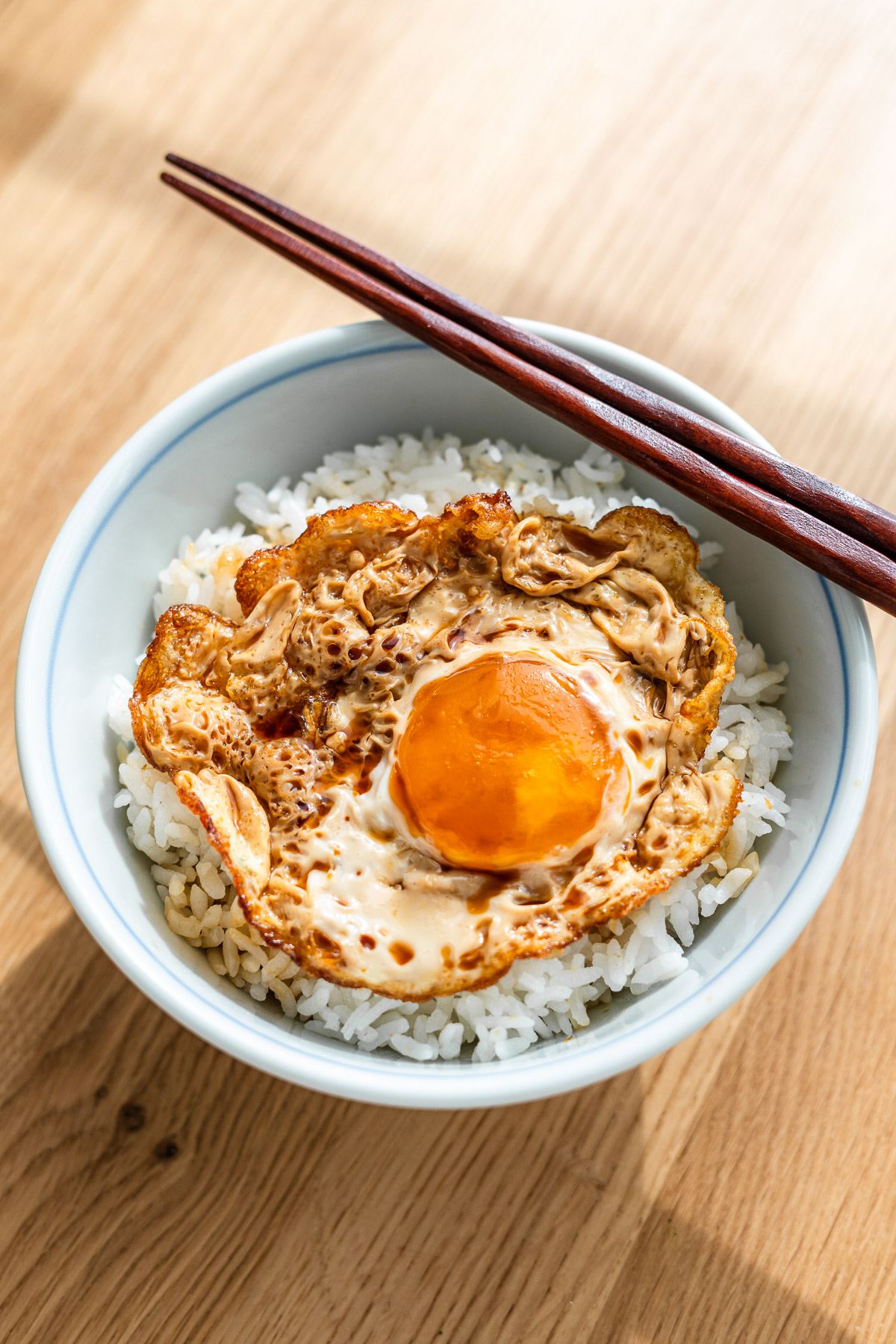 marinated sunny side up fried egg over rice in a blue rice bowl with chopsticks on the side