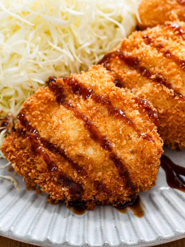 egg katsu on a blue plate with tonkatsu sauce drizzled on top beside a bed of finely shredded cabbage